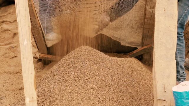 Closeup 4k video of workers sieving sand for house construction. Manual labor scene showing building preparation, material processing, and rural construction work.