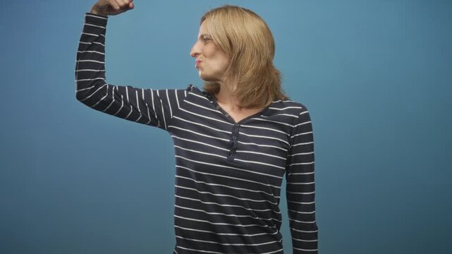 Woman flexes arm and puckers lips while wearing a striped shirt in studio; confidence empowerment strength.