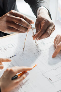 Hands using a compass and pens to mark detailed architectural plans during a collaborative design meeting