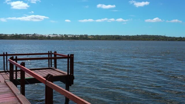 Panoramic view of Lake Joondalup from Neil Hawkins Park viewing platform. Vibrant blue waters under a clear sky with lush green landscape on the horizon