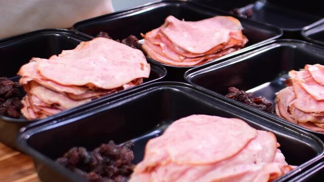 Close up handwork filling the containers with sliced hams and raisins