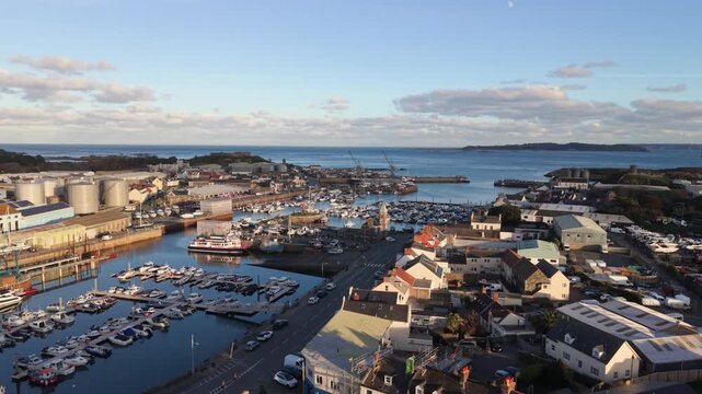St Sampson Guernsey high reveal from the marina backwards over the rooftops of St Sampson in golden afternoon sun with Vale Castle,Herm and Little Russell Channel in the background