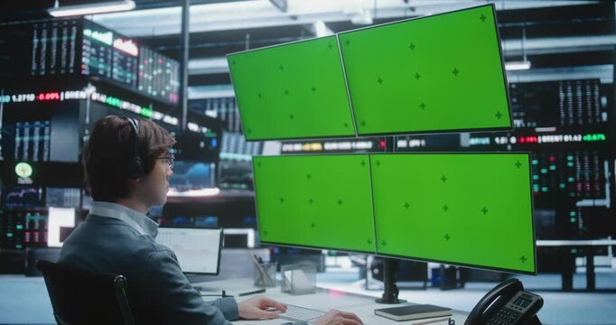 Male Stock Trader With Headset Monitors Multiple Large Green Screen Displays in Modern Stock Exchange Center. Chroma Key Monitors Allow For Customizable Financial Dashboards. Advanced Technology.