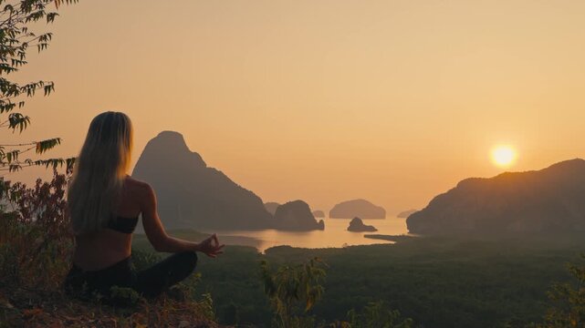 Silhouette of a woman meditating off center while overlooking a bay with towering limestone islands at golden hour