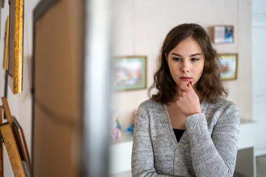 young woman, alone, observes a painting attentively in an art gallery or museum, suggesting she is an art connoisseur, expert, or appraiser.