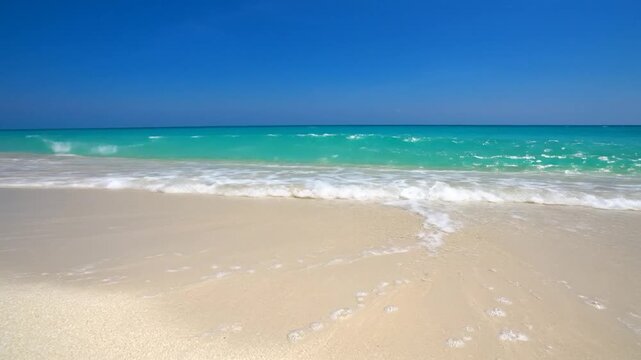 Gentle ocean waves lap onto a pristine sandy beach under a clear blue sky