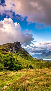 Dramatic landscape of grassy foreground and rocky hills under a cloudy, blue sky