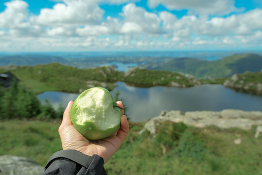Hand holding bitten green apple with mountain lake view in Vidden Trail Norway
