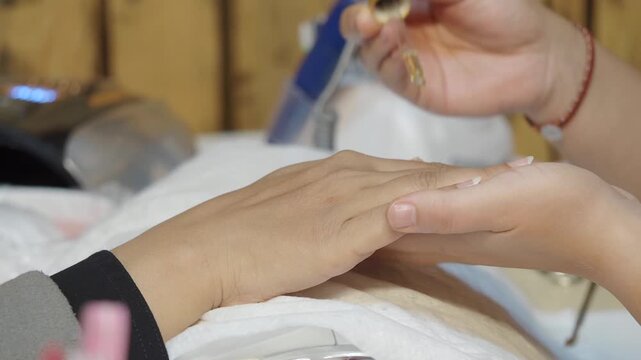 Manicurist applying nourishing cuticle oil on female hand and massaging skin after professional nail treatment in beauty salon.