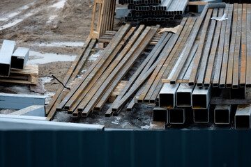 Obraz premium Stacks of steel beams and rectangular metal tubes arranged outdoors on a muddy worksite