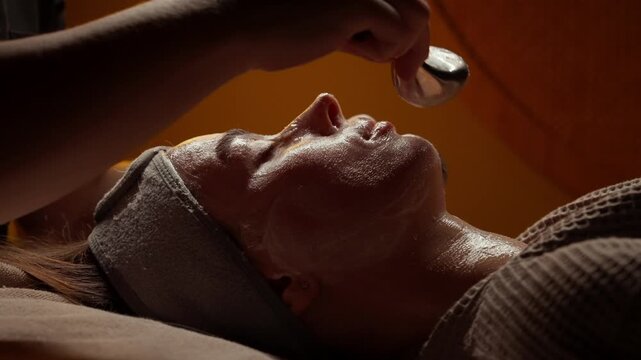 Relaxing facial spa treatment with soothing massage tools and hydrating skincare applied to a woman face and neck in a warm, calming wellness setting