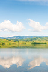 Green mountains and the blue sky with clouds are reflected in the lake. Beautiful summer landscape.