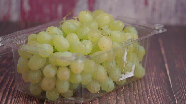 Fresh green grapes in plastic container on wooden table in slow motion.