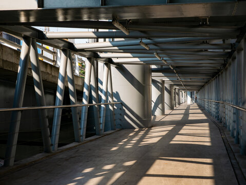 Dramatic perspective of an empty elevated walkway with steel tube roof structure casting striped shadows in golden morning light