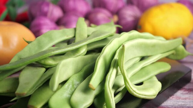 Fresh green flat beans ready for cooking, surrounded by other organic vegetables like potatoes, onions, and lemons in slow motion.