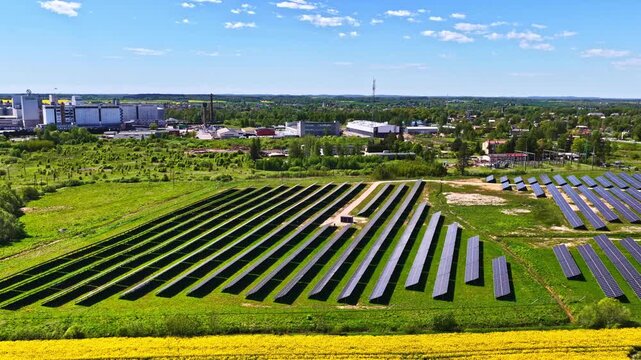An expansive solar array stretches alongside industrial edges and open fields in a verdant rural environment.