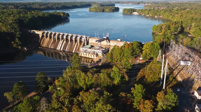 Hydroelectric dam and electrical substation beside reservoir surrounded by forested hills, aerial establishing of renewable energy infrastructure