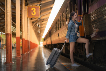 Obraz premium Young woman traveler with suitcase waiting at train station platform, travel and transportation concept.