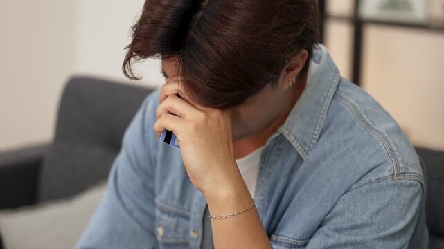 Young Asian Man Feeling Stressed While Using Smartphone and Credit Card