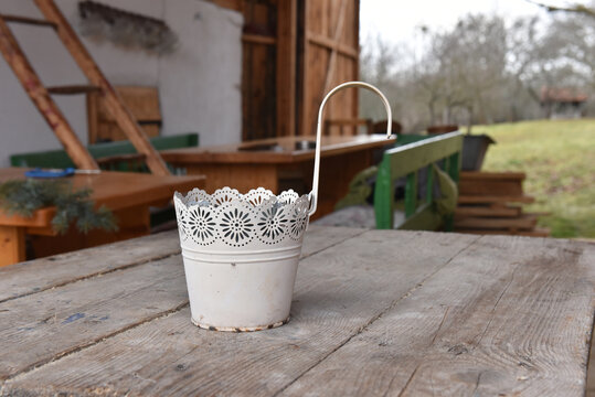 White metal decorative cachepot or hanging planter with a lace-cutout rim on a rustic wooden table