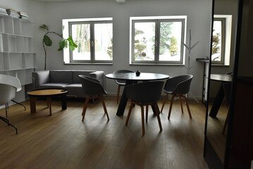 Fototapeta premium Modern minimalist living room featuring grey armchairs a round black dining table and light wood flooring