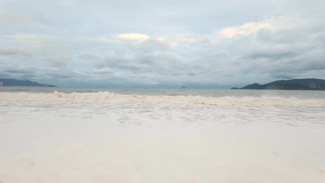 Cloudy beach scene with waves rolling onto shore at sunset in a coastal location