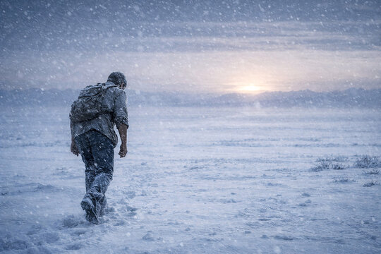 Lone traveler walking through a fierce snowstorm across a frozen plain at sunset with blowing snow cold blue tones and vast winter wilderness conveying endurance isolation survival and adventure