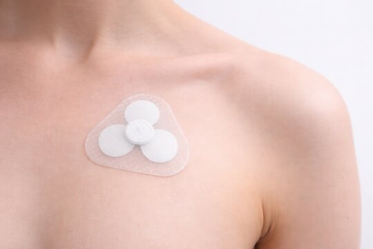 Medical chest patch wearable health monitoring device on human skin close up
