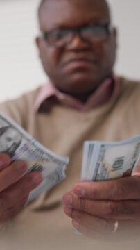 Senior african american male person counting cash, closeup view of hundred dollars banknotes and blurred male face, economy and salary, stingy and greedy man, dream about richness and wealth, portrait