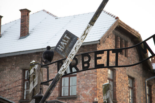 OSWIECIM, POLAND - JANUARY 5, 2025: Detail of the Arbeit Macht Frei sign and a "Halt" warning sign at the entrance to the former Auschwitz I concentration camp in winter.
