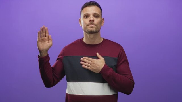 Man placing hand on chest and raising other hand in an oath gesture against a purple studio backdrop; promise sincerity.