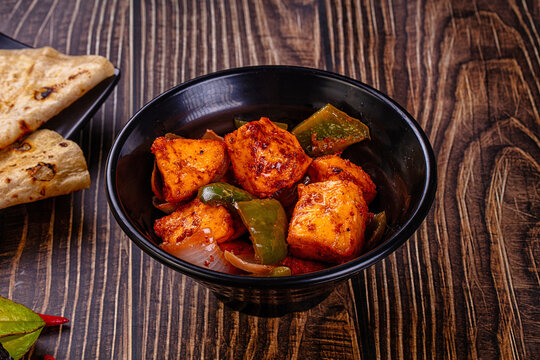 Indian Paneer Tikka Masala inl with Roti bread on a dark wooden table