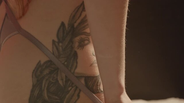 Beautiful extreme close up of a stunning tattoo on the hip of an attractive woman sensually playing with her revealing thong