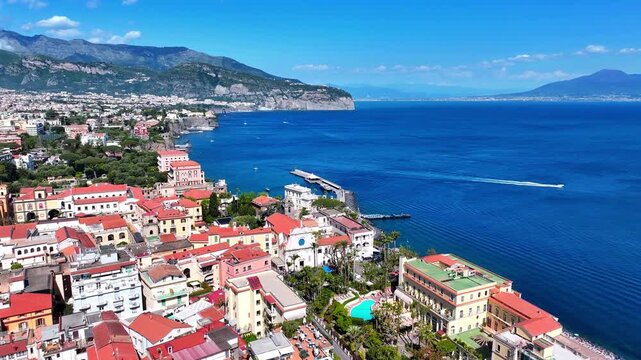 Aerial view over Sorrento on Italy&rsquo;s Sorrentine Peninsula, showing Marina Piccola, cliffside hotels, terracotta rooftops, and the deep blue Bay of Naples on a bright summer day.