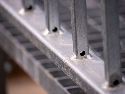 Galvanized steel railing detail with welded joints and vertical bars, including drainage holes for water and moisture, industrial metal construction close-up with shallow depth of field.