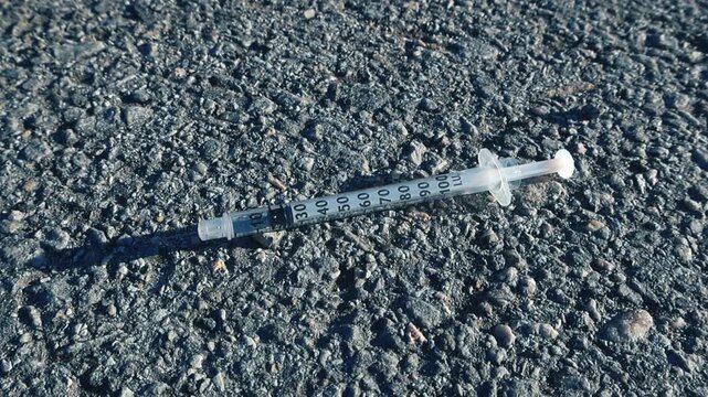 Close up view of a discarded hypodermic syringe lying on the rough asphalt of a street, highlighting issues of drug abuse, addiction, pollution, and public health danger