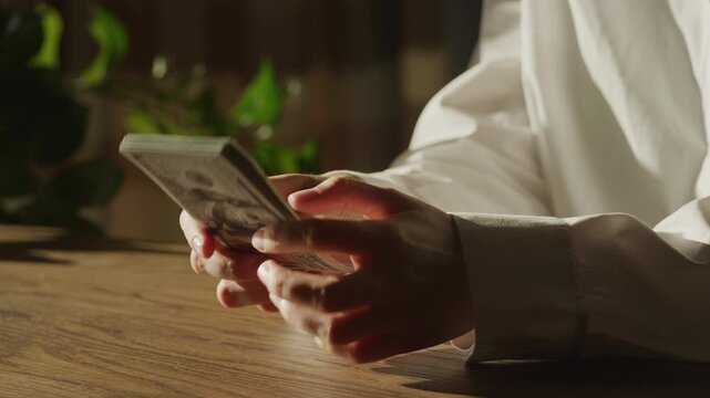 Hands Counting Dollar Bills on Wooden Table