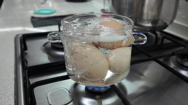 Boiling brown eggs in a clear glass pot on a kitchen gas stove with bubbling water.