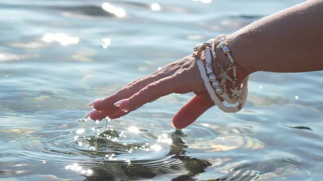 Hand water ocean dipping fingers into clear sparkling sea on a bright sunny summer day with beach jewelry