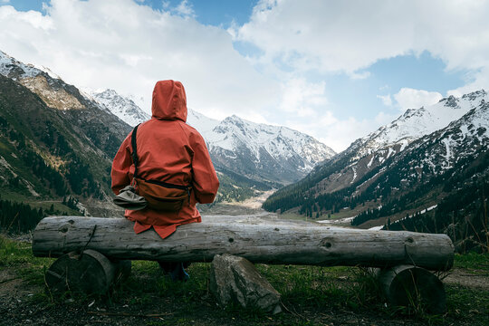 woman in a orange jacket sitting on a bench on a rocky shore on a cloudy day, rear view. The concept of loneliness, melancholy, mental health.