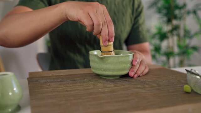 Close up of man preparing matcha by stirring green tea powder in bowl.