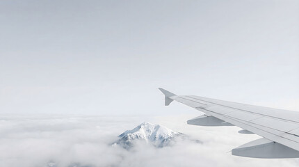 Fototapeta premium Airplane wing flying above white clouds and snow covered mountain peak