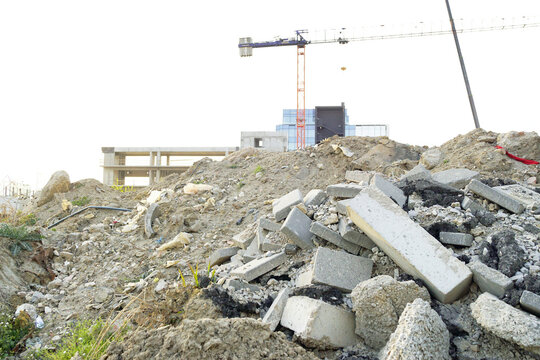 Pile of broken concrete blocks and construction debris with crane in distance. Highlights material lifecycle transition, demolition output reuse, resource recovery, and redevelopment preparation phase