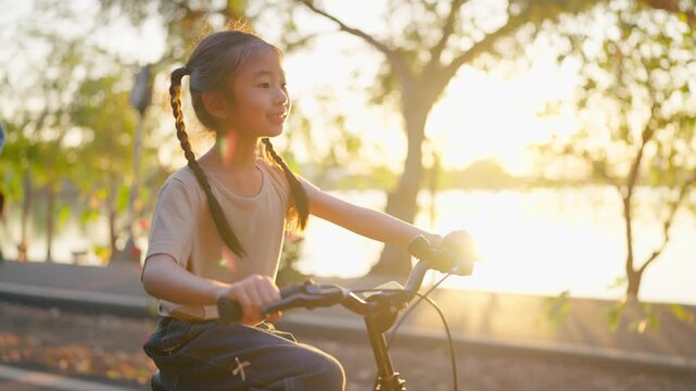 Asian young girl riding bicycle in garden while her parents look after. 