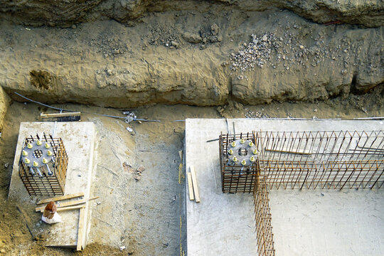 Top view of foundation elements with reinforcement cages and concrete bases inside excavation. Illustrates underground construction stage, structural anchoring system, and base stabilization process.