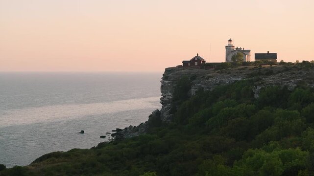 Stora Karls&ouml; lighthouse on cliff at sunrise with soft pink sky and calm Baltic Sea, Gotland, Sweden
