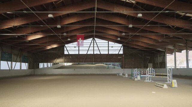Empty indoor horse riding arena with sand ground and show jumping obstacles under a wooden roof