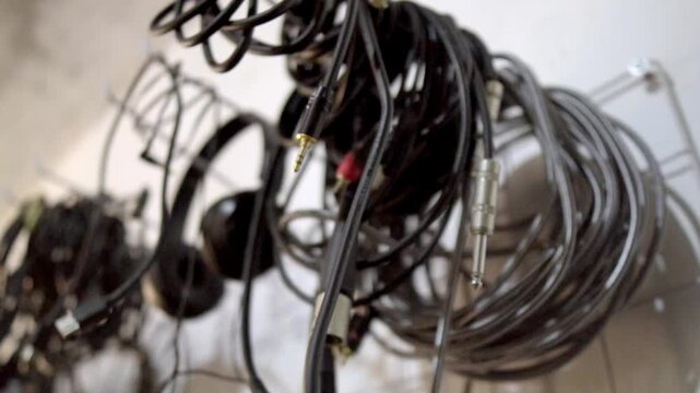Close up of various tangled audio cables, jack connectors, and headphones hanging in a music recording studio.
