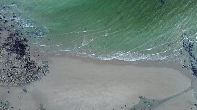 Slow motion rising drone shot of waves crashing along rugged sandy coastline at Fairlight Cove, East Sussex, UK.