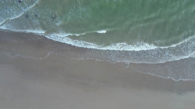 Rising drone shot capturing waves breaking on sandy beach at Fairlight Cove, East Sussex, UK in bright spring daylight.